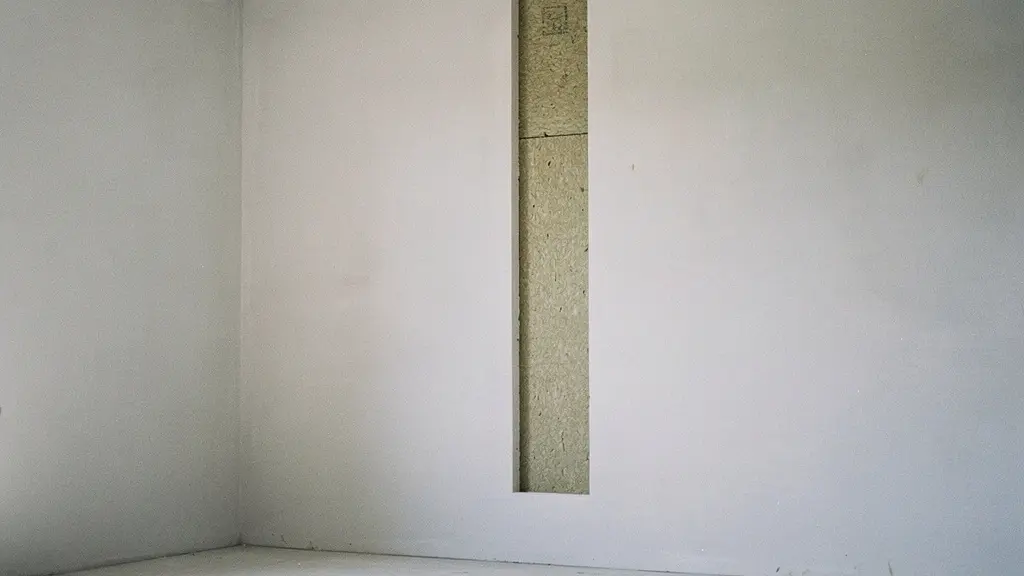 Interno minimalista con una parete in ristrutturazione che mostra un sottile strato isolante e una finitura pulita, con ampio spazio vuoto e nessun testo visibile.